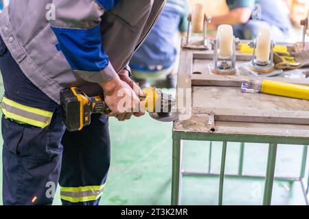 Hands of worker grinding a cart base wheel for install in workshop. Stock Photo