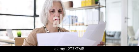 Serious grey haired woman studies reports sitting at desk Stock Photo
