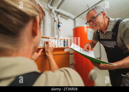 Team of heating engineers checks a old gas heating system with a paper instruction at a boiler room in a house. Gas heater replacement obligation conc Stock Photo