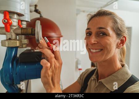 Happy female heating engineer checks gas thermostat at a boiler room with a old gas heating system. Gas heater replacement obligation concept image Stock Photo