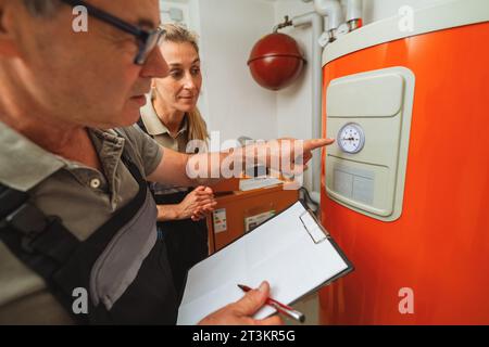 Team of heating engineers checks a old gas heating system thermostat, holding a Clipboard with checklist at a boiler room in a house. Gas heater repla Stock Photo