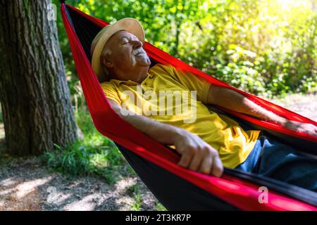 Elderly Man with straw hat Relishing a Peaceful Nap in a Hammock in the park Stock Photo