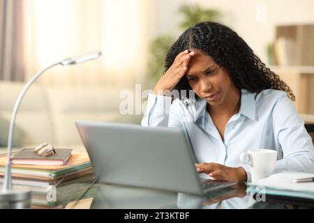 Worried black tele worker checking bad news on laptop at home Stock Photo