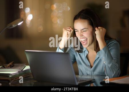 Excited worker checking laptop content celebrating online in the night at homeoffice Stock Photo
