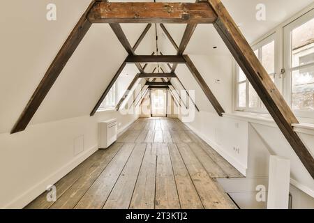 an attic with wood flooring and exposed beams on the ceiling, white walls are visible in the room to the right Stock Photo