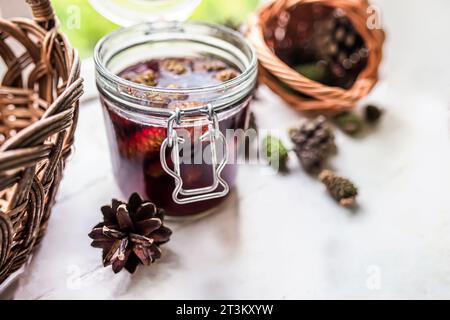 jar of pine cone jam sits on a wooden table, surrounded by a basket of fresh pine cones. The jam is a golden yellow color, with a thick, syrupy consis Stock Photo
