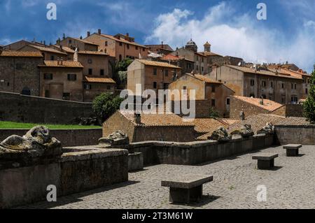 Headless effigies of Ancient Etruscans recline on sarcophagus lids, now laid along a low Piazza wall in Tuscania, Lazio, Italy.  Tuscania’s old town rises behind.  Tuscania was formerly the Ancient Etruscan city of Tuscana.  It lies about 80 km (50 miles) north-west of Rome. Stock Photo