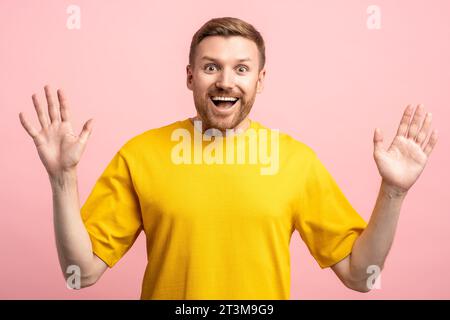 Amazed glad fun filled middle-aged bearded man with hands up looking at camera on pink background Stock Photo