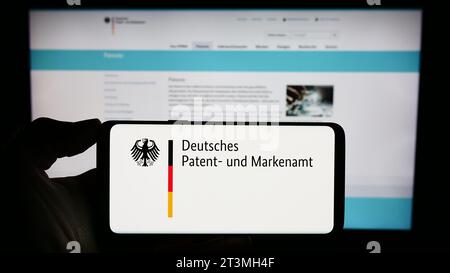 Person holding cellphone with logo of German agency Deutsches Patent- und Markenamt (DPMA) in front of webpage. Focus on phone display. Stock Photo