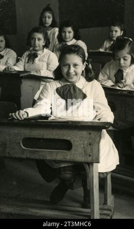 Class photo of girls with apron and bow in the classroom, Italy 1960s Stock Photo