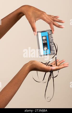 Side view of anonymous young ethnic female while standing in room and demonstrating vintage cassette with spilled out tape in manicured finger hands a Stock Photo