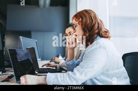 A diverse team of professionals collaboratively discussing and programming software in a modern office. Men and women are seen sitting around a table Stock Photo