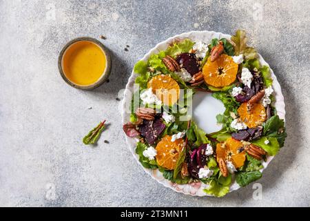 Christmas appetizer. Christmas wreath salad with beetroot, tangerines, feta cheese and pecans on the festive table. View from above. Stock Photo