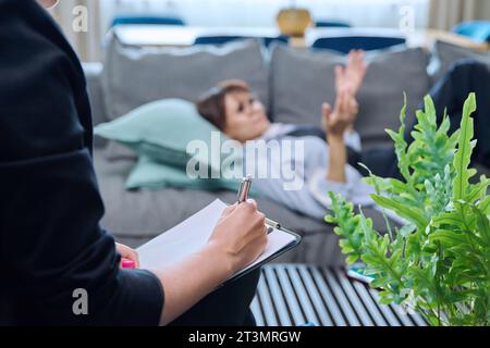 Close-up of female psychologist's hands with clipboard making notes, in therapy Stock Photo