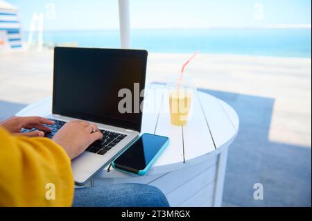 Rear view of a laptop with blank black mockup screen and businesswoman, freelancer or copywriter typing text on keyboard, telecommuting sitting at tab Stock Photo
