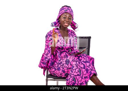 portrait of a beautiful young businesswoman wearing traditional loincloth sitting on a chair using a digital tablet while gesturing finger.. Stock Photo