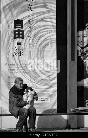 Black And White Photo Of A Elder Chinese Man Holding A Baby At The 798 Art Zone, Dashanzi Art District, Beijing, China. Stock Photo