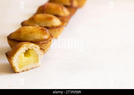 Pasticciotto leccese pastry filled with egg custard cream, typical sweet from Lecce, Italy. Pieces of baked pasticiotto on a white table in a line, ap Stock Photo