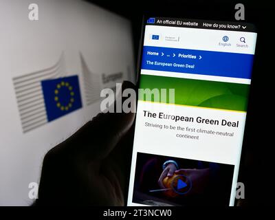 Person holding cellphone with webpage of EU institution European Commission (EC) in front of logo. Focus on center of phone display. Stock Photo