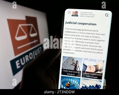 Person holding smartphone with webpage of EU Agency for Criminal Justice Cooperation (Eurojust) with logo. Focus on center of phone display. Stock Photo