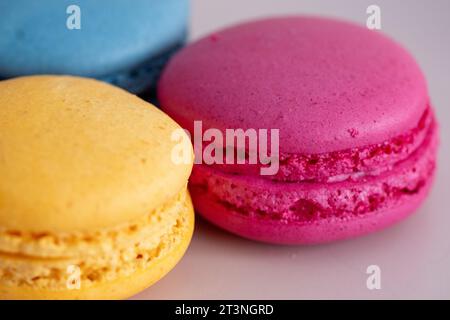 three different colored macarons on a pink plate on a blue background Stock Photo
