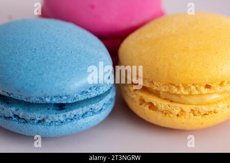 three different colored macarons on a pink plate on a blue background Stock Photo