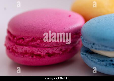 three different colored macarons on a pink plate on a blue background Stock Photo