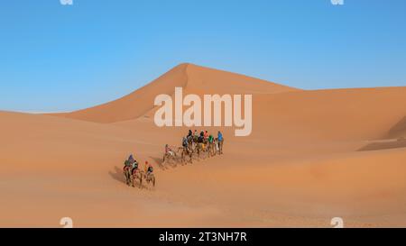 Sahara Desert, Morocco - 13 September 2022: Tourists on a camel ride across the sand dunes guided by a Berber man, a classic Sahara Desert tourism exp Stock Photo