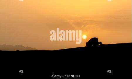 Silhouette of unidentified muslim Berber man praying on sand dunes at ...