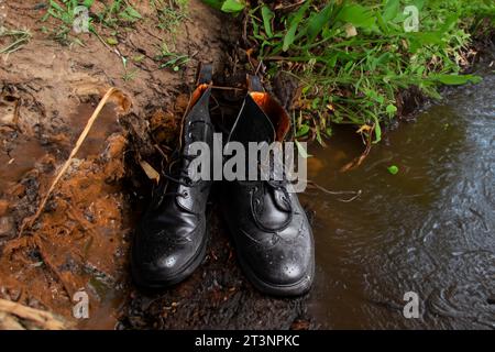 Pair of black leather men's boots left on the muddy edge of a rivier Stock Photo