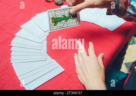 top view of unrecognizable caucasian tarot reader woman, sitting starting therapeutic reading, taking out and turning over card from deck and placing Stock Photo