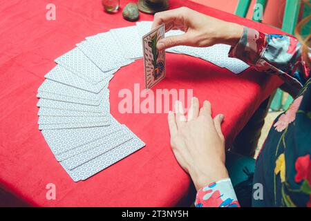 top view of unrecognizable caucasian tarot reader woman, sitting starting therapeutic reading, taking out and turning over card from deck and placing Stock Photo