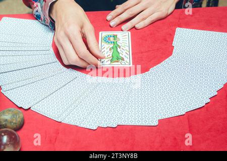 top view of unrecognizable caucasian tarot reader woman, sitting starting therapeutic reading, taking out and turning over card from deck and placing Stock Photo