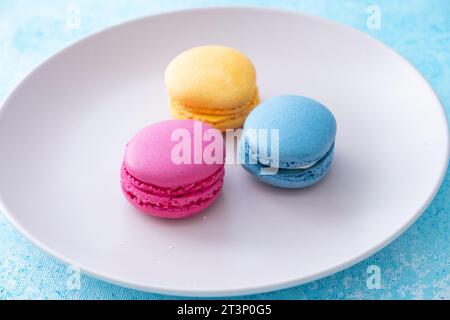 three different colored macarons on a pink plate on a blue background Stock Photo