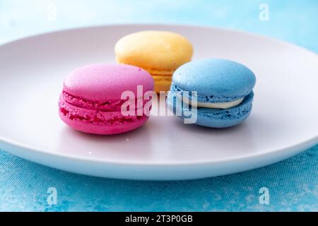 three different colored macarons on a pink plate on a blue background Stock Photo