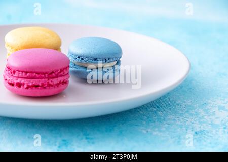 three different colored macarons on a pink plate on a blue background Stock Photo