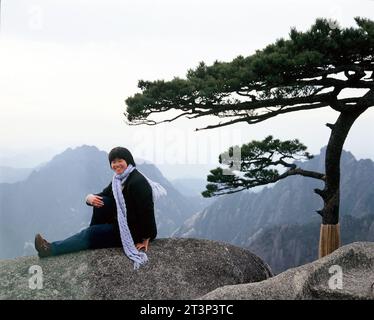 China. Anhui. Huangshan mountains. Chinese young woman sitting on rock. Stock Photo