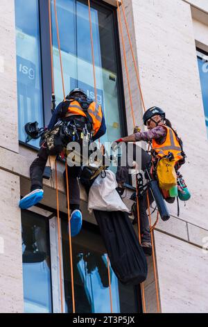 LONDON, UK - August 25, 2023: Construction workers hanging from ropes sealing carpentry on a facade Stock Photo