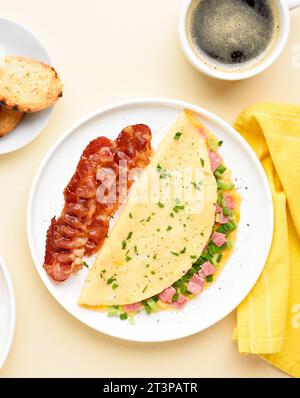 Stuffed omelette with ham and green onion and cup of coffee over light background. Tasty healthy meal for breakfast. Top view, flat lay. Stock Photo