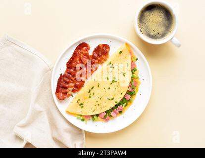 Stuffed omelette with ham and green onion and cup of coffee over light background. Tasty healthy meal for breakfast. Top view, flat lay. Stock Photo