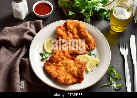 Pork schnitzel with lemon and leaves of parsley on white plate over brown stone background. Close up view Stock Photo