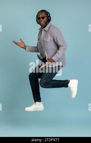 Carefree guy listens lively music modern stereo headphones jumping up to air with happy face Stock Photo
