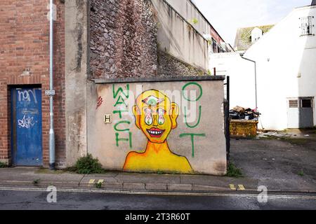 'Watch out' graffiti art of eyeballs falling out of yellow persons head along Lower Union Lane backstreet in Torquay Stock Photo