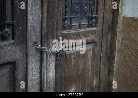 Closeup of a wooden door of an old house that is closed with a padlock and chain to prevent squatters from entering Stock Photo