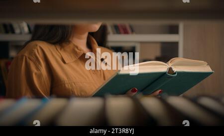 Unrecognizable woman reading book in university library near bookcase smart female girl college student teacher read textbook literature prepare for Stock Photo