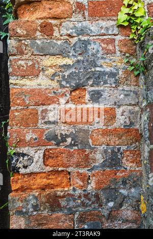 Section of an old red brick wall. There are cracks and damage and some ivy in the corner Stock Photo