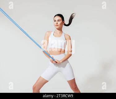 Healthy slim woman in white sports clothes practicing with resistance band in studio Stock Photo