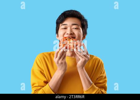 Young Asian man eating tasty pizza on blue background, closeup Stock Photo