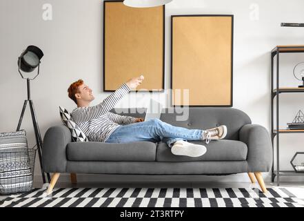 Young man with laptop switching on air conditioner at home Stock Photo
