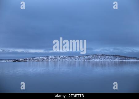 Panoramic view of Torneträsk lake with snowy mountain under a dark cloudy sky in winter in the Abisko National Park Stock Photo